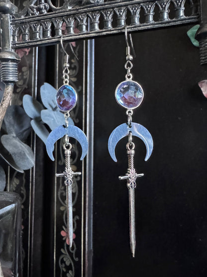 Beautiful blue to purple ombre gemstone earrings with silver crescent moons and swords, dangle on display.