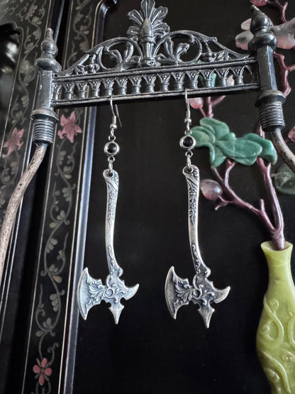 A pair of sterling silver axe earrings feature an ornate detail on the blade and black zirconia connectors.