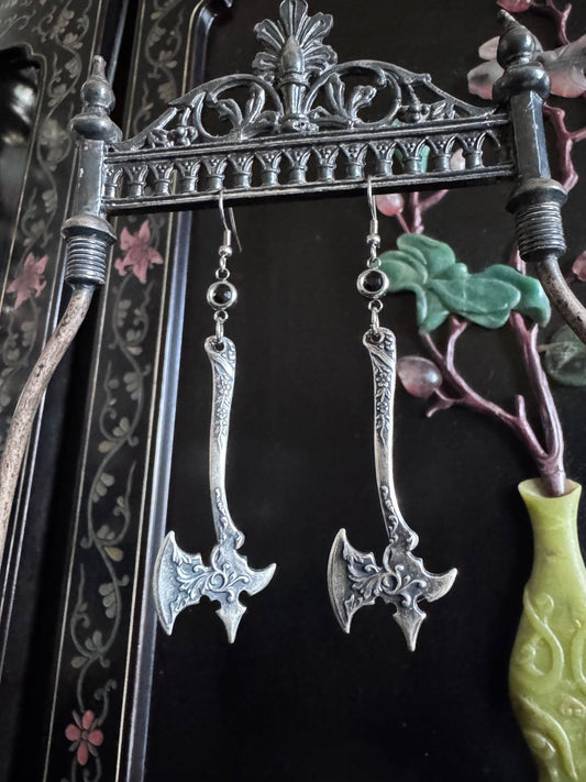 A pair of sterling silver axe earrings feature an ornate detail on the blade and black zirconia connectors.