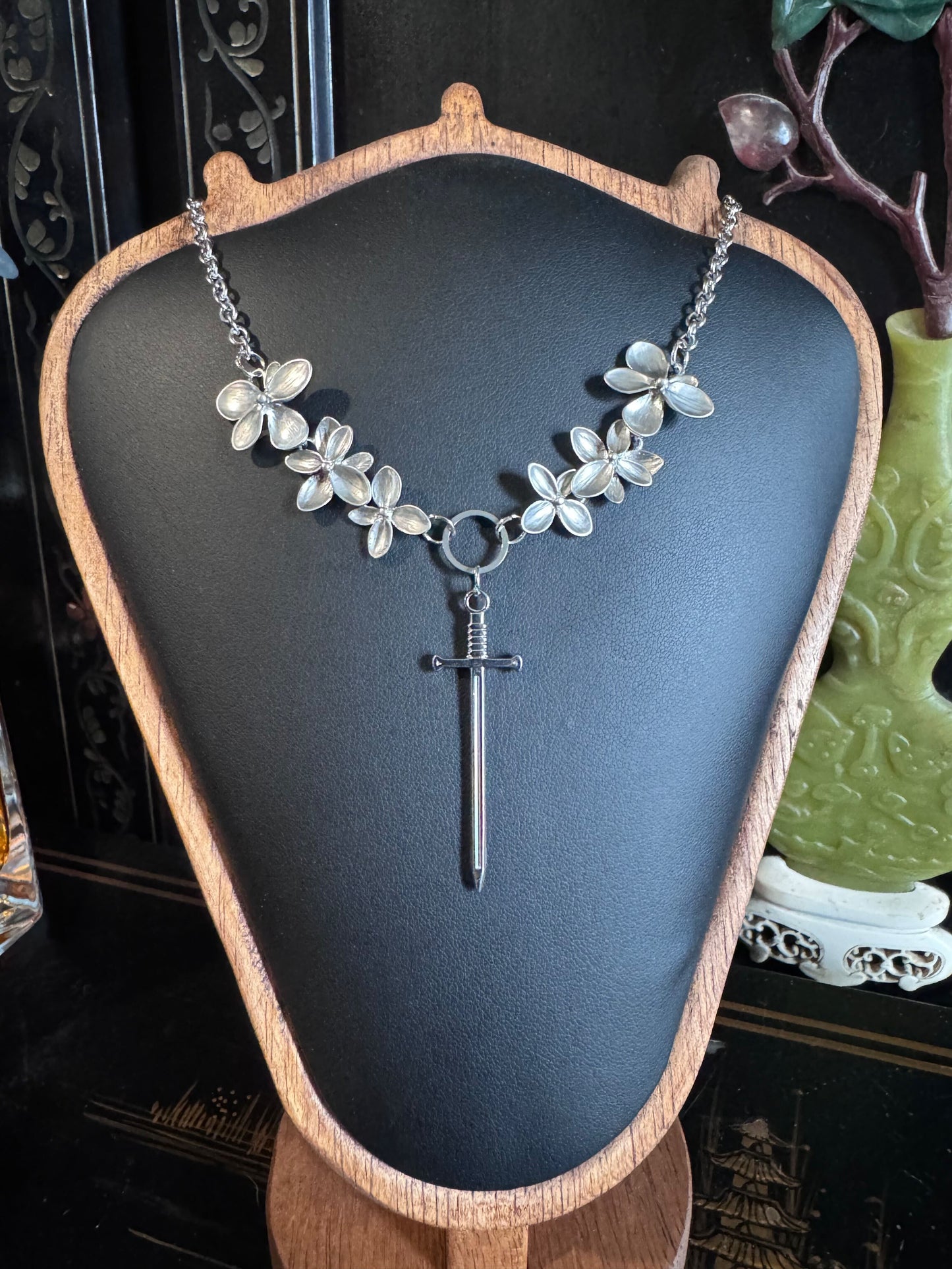 A silver chain necklace features cascading flowers and a sword pendant.