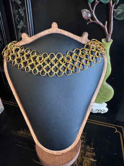 A thick, classic woven gold chainmail choker rests on a black background display.