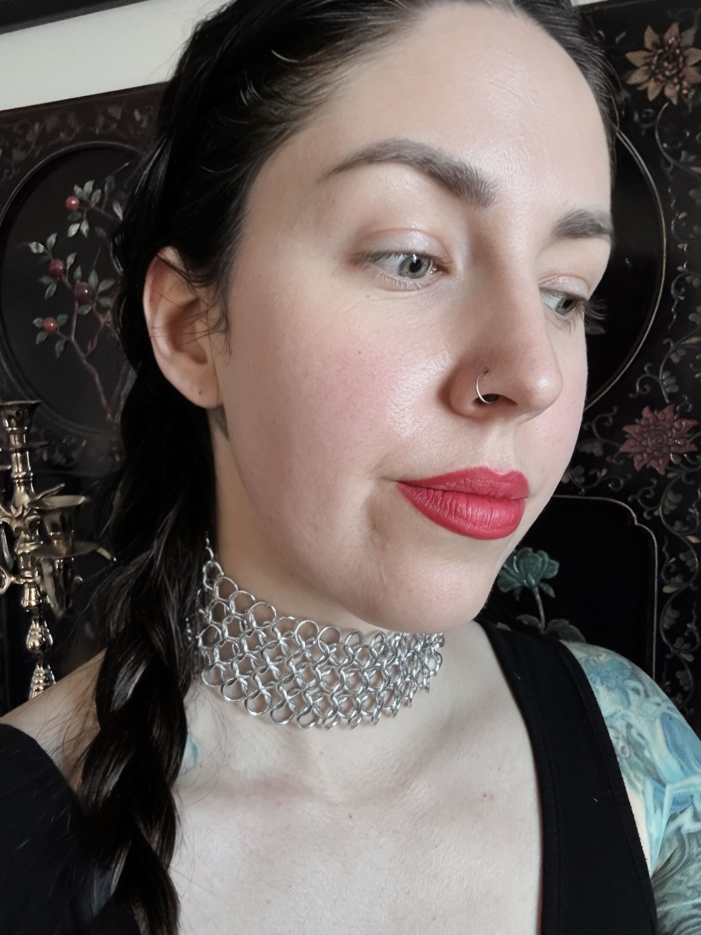 A woman wears a thick chainmail woven choker that envelops the majority of her neck.