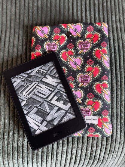 A kindle e-reader sleeve featuring a coquette heart design with a kindle resting on top.