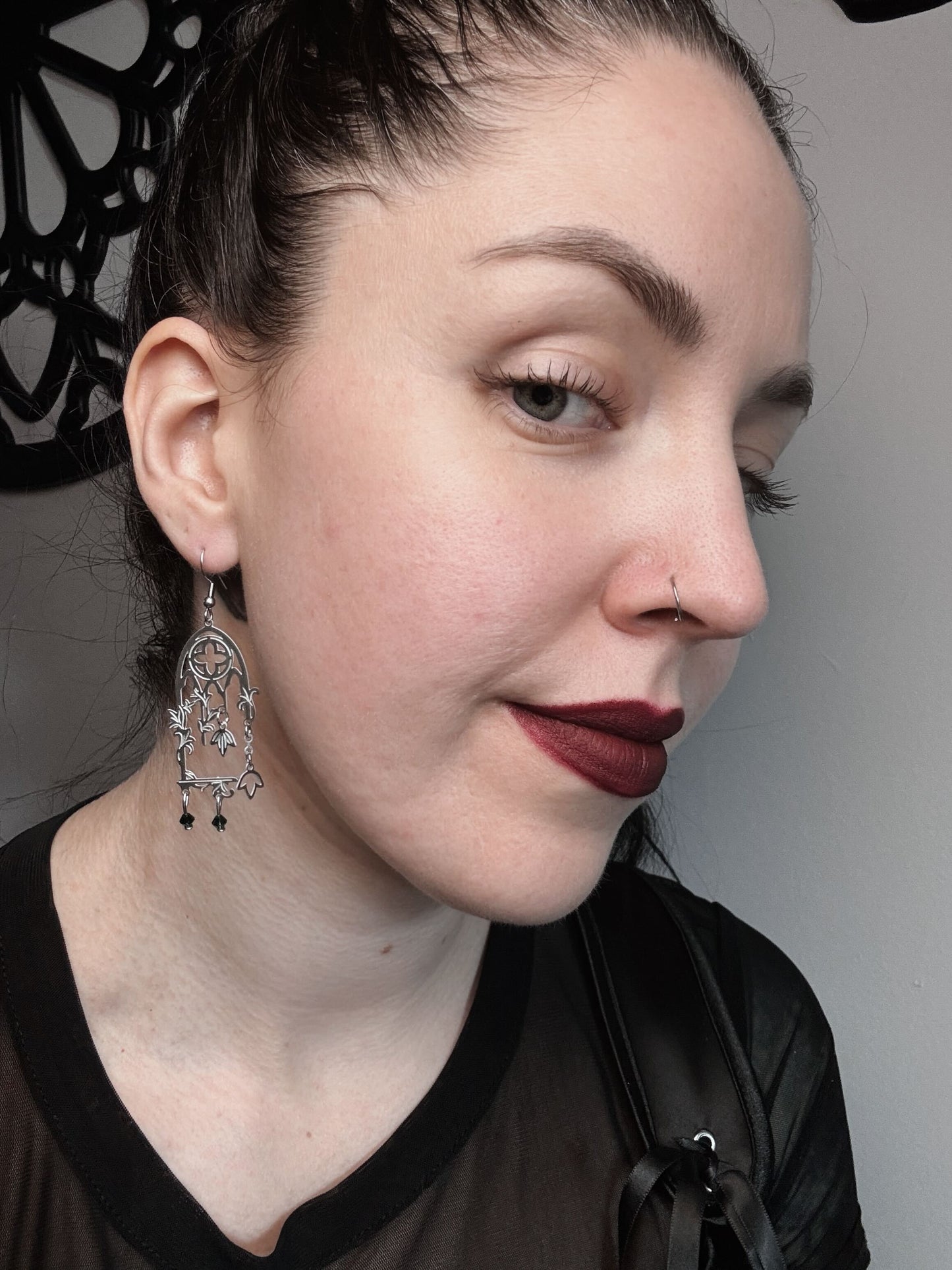 A woman wears a pair of cathedral windows that have vine and emerald bead details.