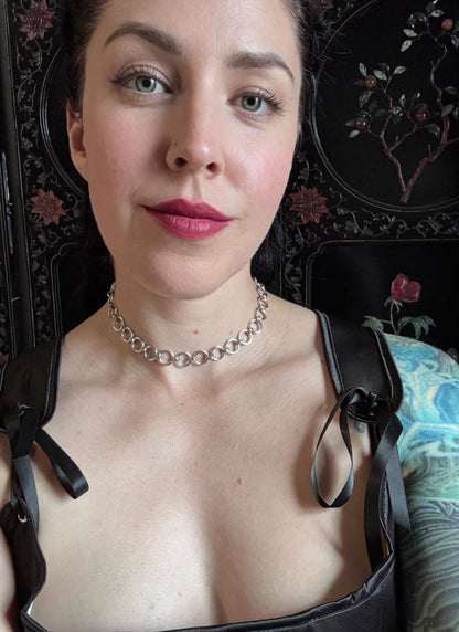A woman wears a delicate silver chainmail necklace and a black corset.